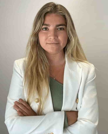 A portrait of a woman in a white blazer and green top, arms crossed, looking at the camera.