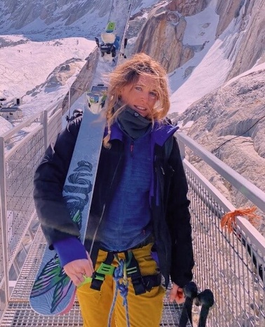 A person holding a snowboard on a bridge with icy mountain background.