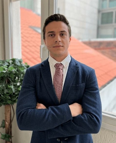 A man in a blue suit and red tie standing confidently with his arms crossed in front of a window.