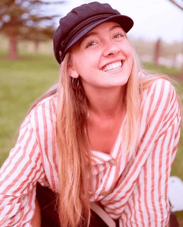 A smiling woman wearing a black cap and a striped shirt sitting outdoors.