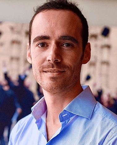 Portrait of a smiling man in a blue striped shirt with a blurred background.