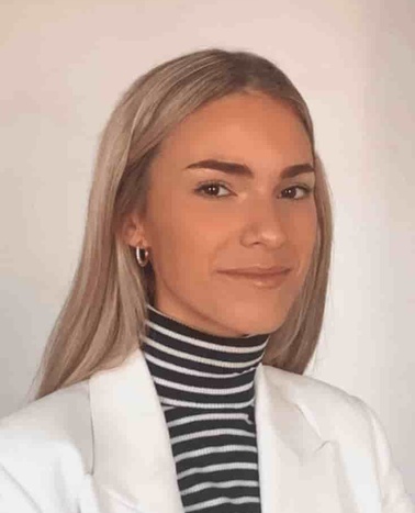 A portrait of a smiling woman with blonde hair, wearing a white jacket and a black and white striped turtleneck.
