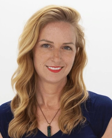 A portrait of a smiling woman with long wavy blonde hair wearing a blue shirt and a necklace.