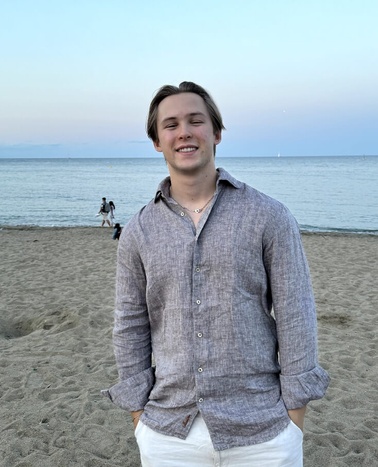 A young man smiling on a sandy beach during the evening.