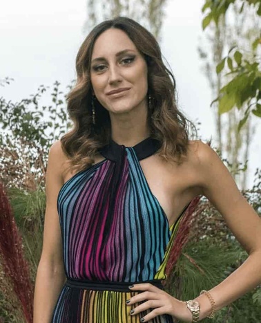 A woman in a colorful striped dress standing in a garden.