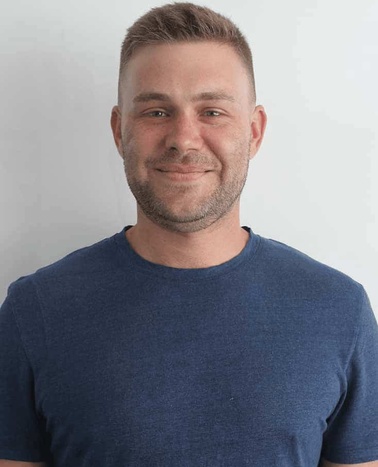 A portrait of a smiling man wearing a blue t-shirt against a white background.