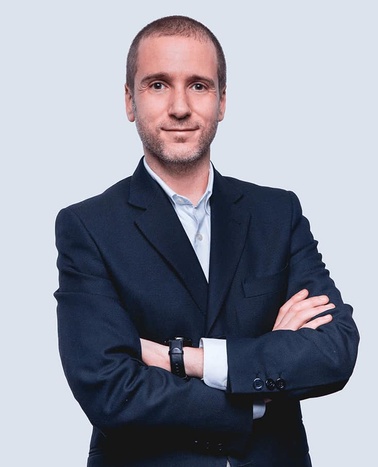 A professional man in a suit with crossed arms smiling at the camera.
