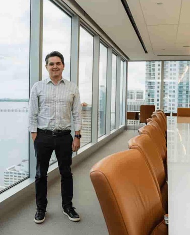 A man standing next to a window in a modern office overlooking the city.