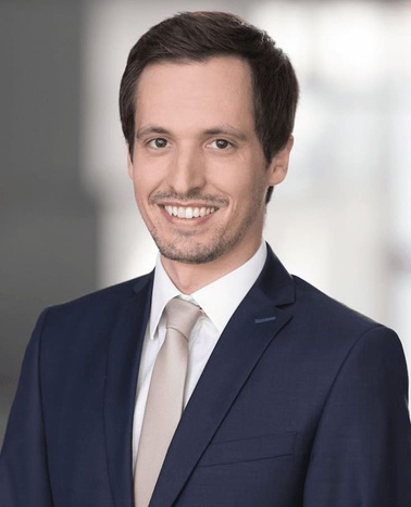 A professional portrait of a smiling man wearing a blue suit and tie.