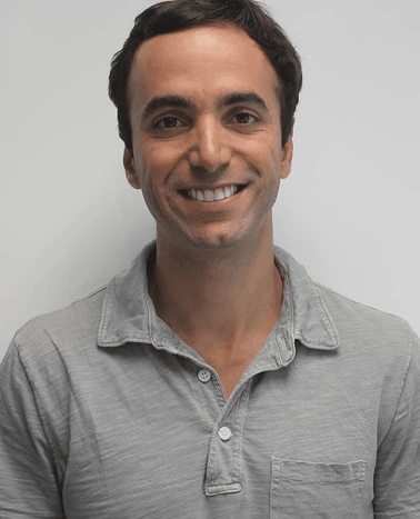 A smiling man wearing a gray collared shirt against a plain white background.