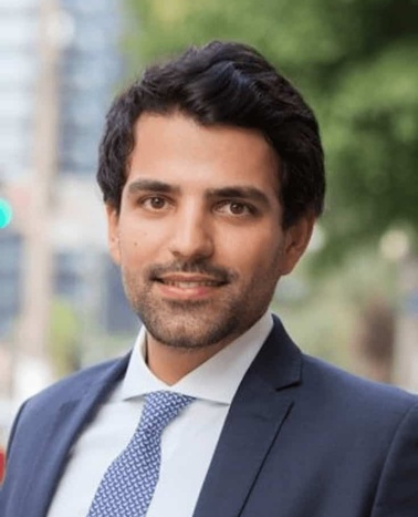 A portrait of a smiling man in a business suit and tie with an urban background.