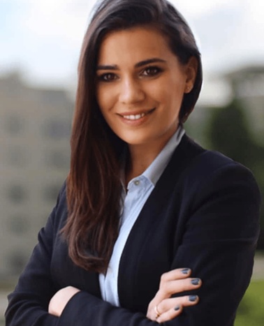 Portrait of a smiling professional woman in a dark suit with crossed arms standing outdoors.