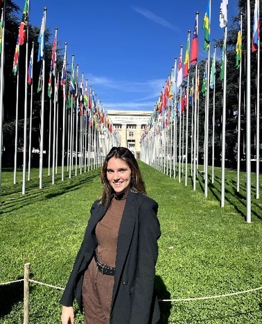 A woman smiling in front of a row of international flags outside a building.