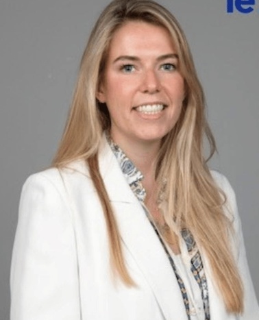 A portrait of a smiling woman in a white blazer with a patterned blouse.