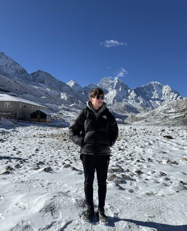 A person standing in a snowy landscape with mountains in the background.