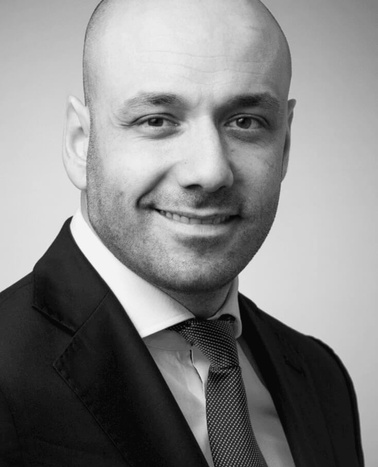 Black and white portrait of a smiling bald man wearing a suit and tie.