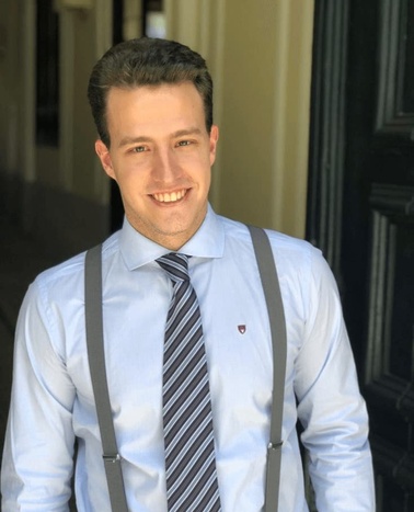 A smiling man in a suit with suspenders standing in front of a doorway.