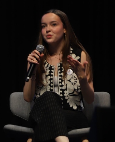 A woman sitting on a chair speaking into a microphone during an event.