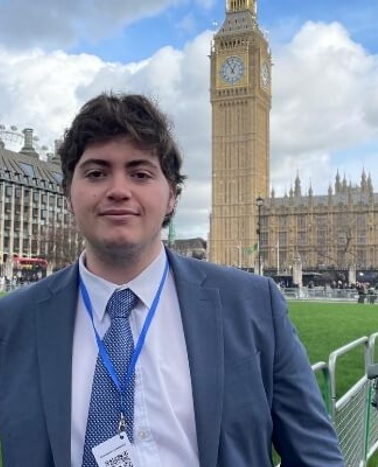 A man in a suit with a lanyard standing in front of the Big Ben in London.