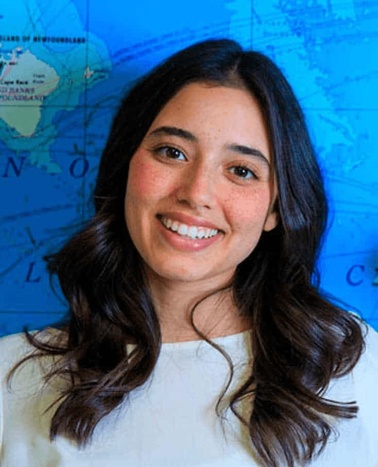 A portrait of a smiling woman with long hair, standing in front of a world map.