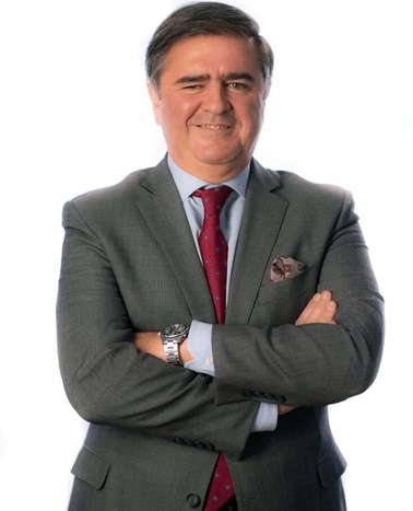 A man in a grey suit and red tie smiling at the camera with crossed arms