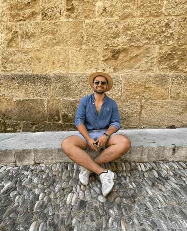 A man in a straw hat sitting on a stone ledge against a textured stone wall.