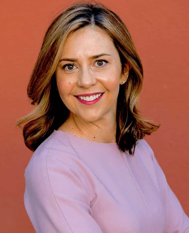A smiling woman with medium-length hair, wearing a pink blouse, standing against a red background.