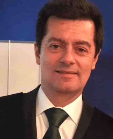 A man in a dark suit with a green tie smiling at the camera.
