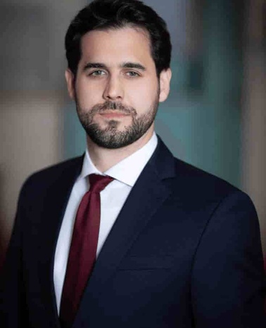 Portrait of a man in a dark suit and red tie looking at the camera.