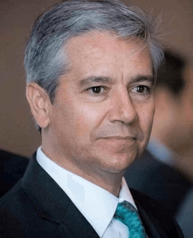 Portrait of a middle-aged man with gray hair, wearing a dark suit and a turquoise tie.