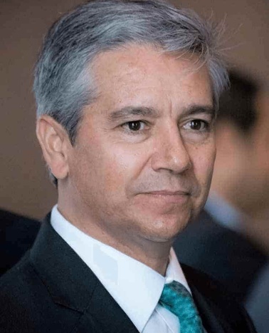 A mature man with gray hair wearing a suit and a turquoise tie