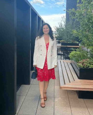 A woman in a red dress and white jacket standing on a rooftop garden.