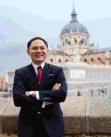 A man in a business suit smiling with his arms crossed in front of a historical dome building.