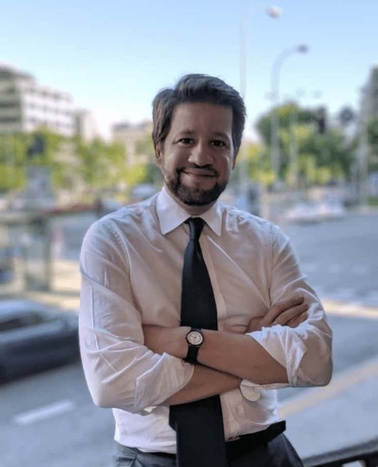 A man in a white shirt and tie smiling confidently in an urban setting.