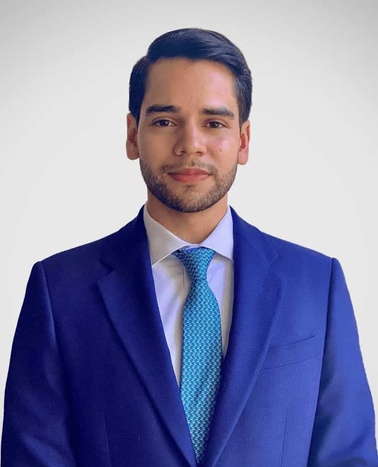 A professional portrait of a young man in a blue suit with a turquoise tie.