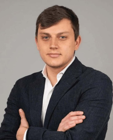 A professional portrait of a young man in a suit with arms crossed.