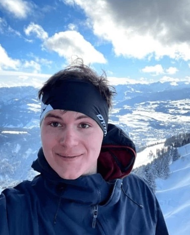 A person smiling at the camera with a snowy mountain landscape in the background.