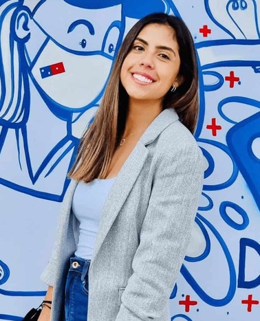 A smiling young woman standing in front of a colorful mural with cartoon-style artwork.