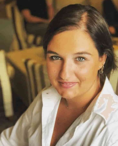 A portrait of a woman with short dark hair wearing a white shirt, smiling at the camera in a softly lit indoor setting.
