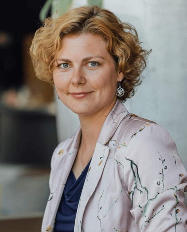 A portrait of a woman with short curly hair, wearing a floral blazer and a dark top, looking at the camera.