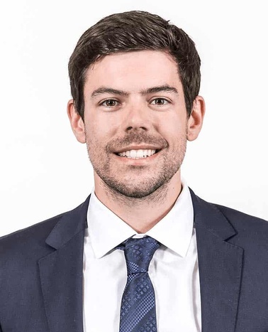 A young man in a suit and tie smiling against a plain white background.