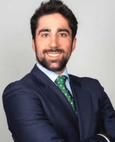 A professional portrait of a smiling man wearing a blue suit and green tie.