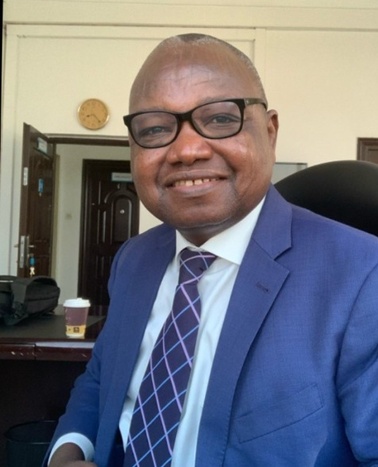 A man in a blue suit and purple tie smiling in an office setting.