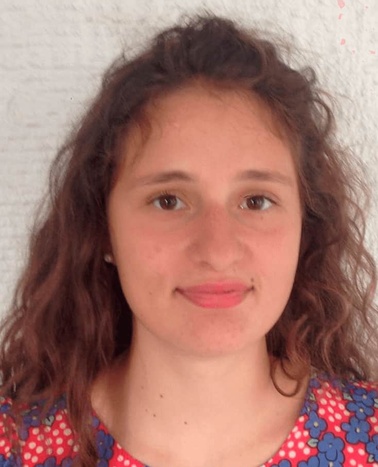 Portrait of a young woman with curly hair wearing a blue and red floral dress against a white background.