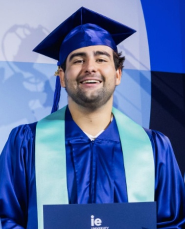 A graduate proudly poses in a blue cap and gown holding a diploma.