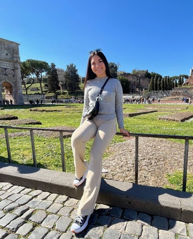 A young woman poses confidently in a sunny outdoor setting near ancient ruins.