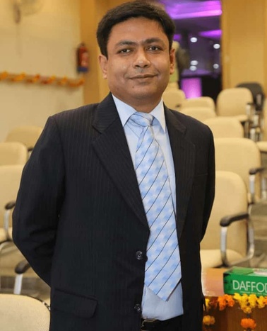 A man in a business suit with a tie stands smiling in a conference room setting.
