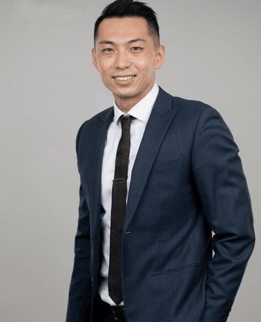A professional portrait of a smiling man dressed in a dark suit and tie.