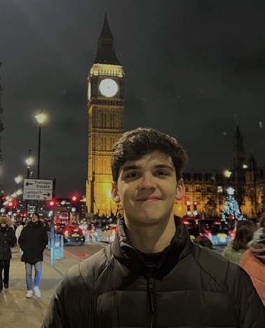 A young man smiling in front of Big Ben at night.
