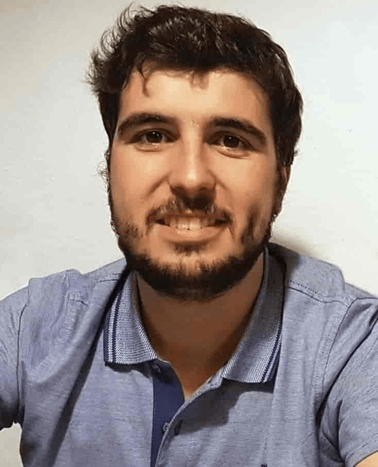 A portrait of a smiling man with dark hair and a beard, wearing a blue polo shirt.